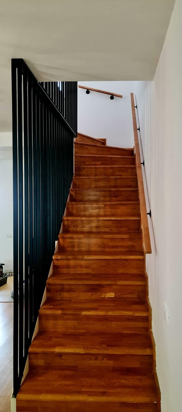Scară interioară din lemn cu balustradă neagră și mână curent din lemn.