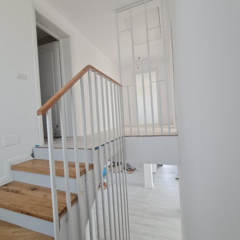 Scară interioară modernă cu balustradă albă și trepte din lemn în casă nouă.