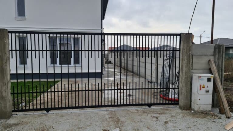 Poartă de grădină din metal negru, montată pe șine, cu caseta de control în dreapta.