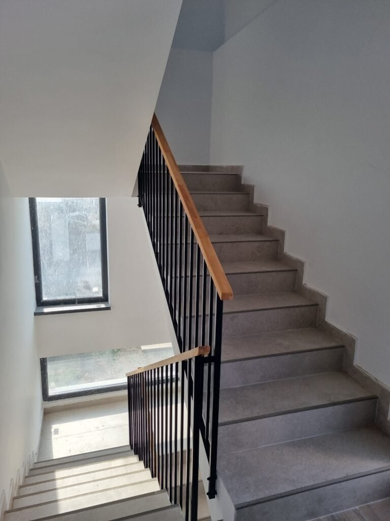 Scară interioară cu balustradă din metal și trepte din beton, într-un spațiu luminos și aerisit.