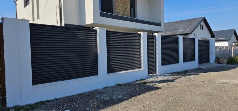 Perete exterior modern cu obloane negre și gard alb pentru intimitate.