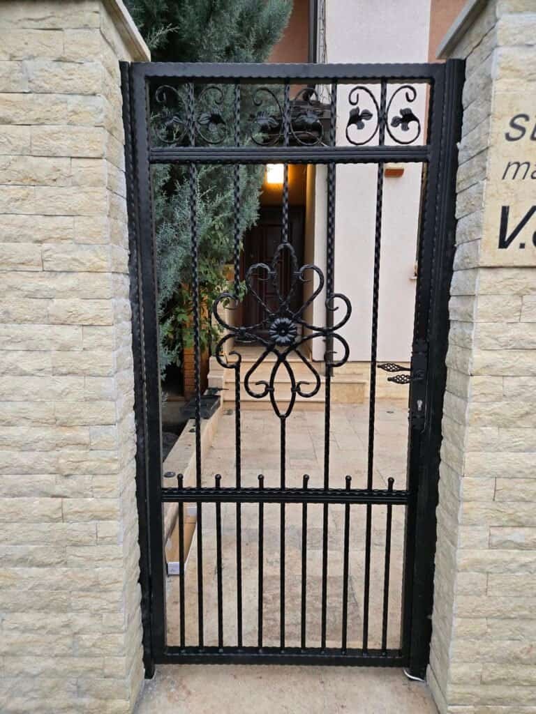 Poartă de grădină din fier forjat negru, cu design ornamental, pentru acces sigur și elegant în curt.