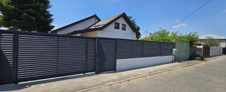 Poartă metalică neagră și gard în fața unei case rezidențiale.