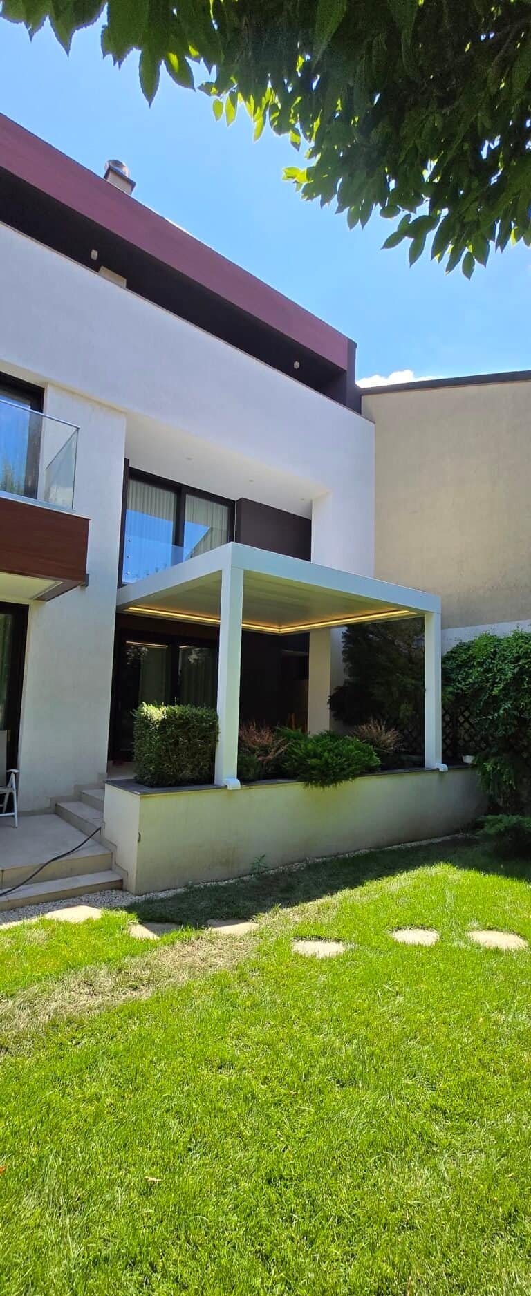 Casă modernă cu terasă și grădină verde, design contemporan și spațiu exterior plăcut.