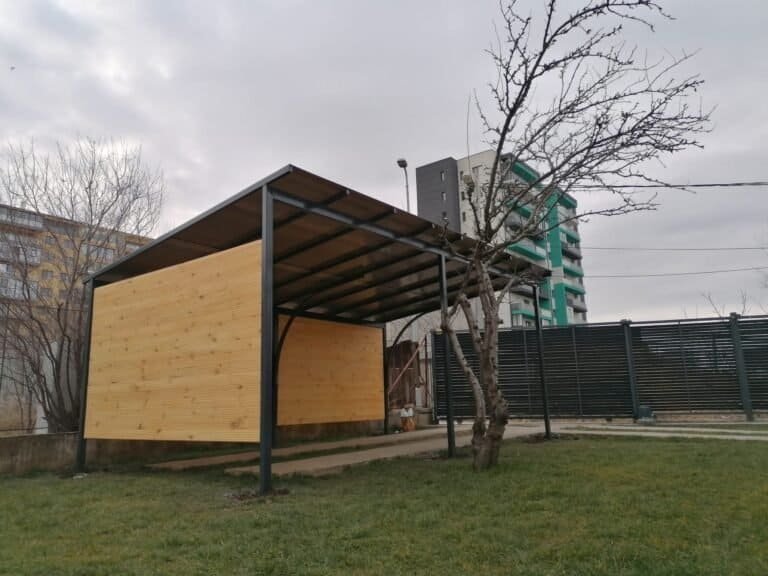 Adăpost exterior cu structură de lemn și acoperiș metalic, ideal pentru protecție și depozitare în g.