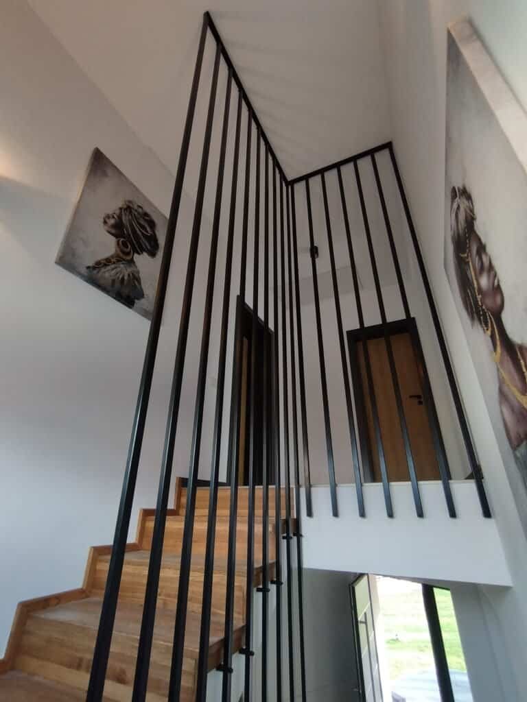 Scară interioară modernă cu balustradă din metal negru și trepte din lemn natural.
